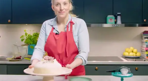 Kvinna med röd förkläde presenterar en marsipantårta. Ett perfekt marsipan recept för firande.