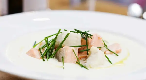 En krämig soppa med bitar av confiterad lax och vit fisk, toppad med färsk gräslök.