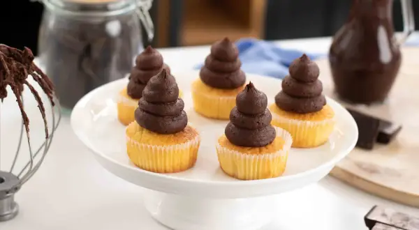 Fem cupcakes med chokladganache, perfekt för ett enkelt ganache recept. Ingredienser för bakning syns i bakgrunden.