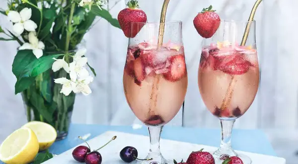 Två glas med drink med gin och prosecco, fyllda med is, jordgubbar och körsbär. Garnerade med jordgubbar och serverade med citroner och blommor.