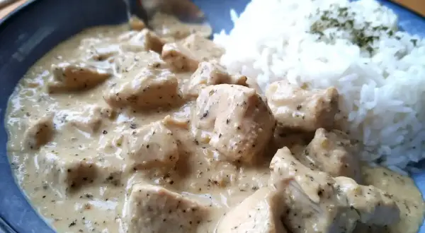 En krämig sås till kyckling och ris, med bitar av kyckling i en len sås. Riset är toppat med lite grön krydda.