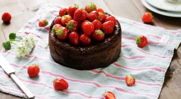 En kladdkaka med nutella, toppad med färska jordgubbar, ligger på en randig duk.