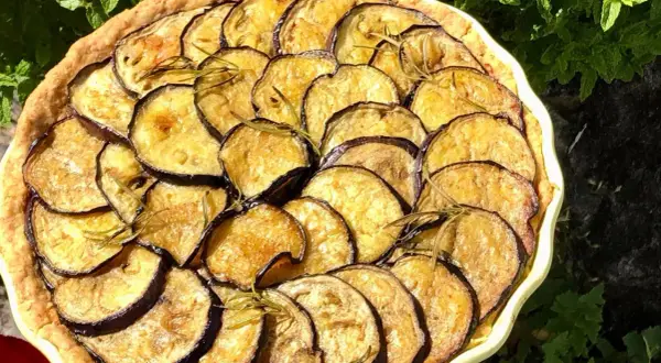 En paj med gyllene, stekt aubergine och rosmarin, vackert arrangerad i en ljusgul form.