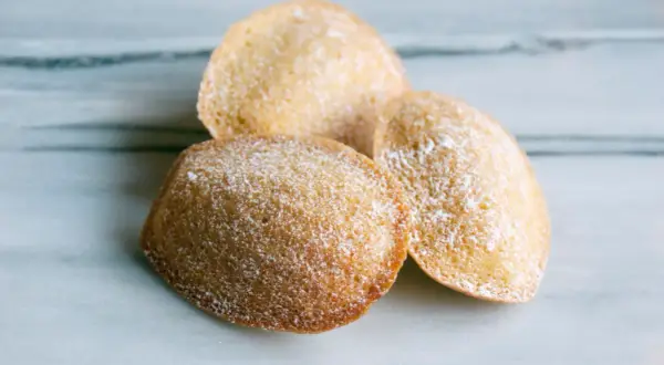 Tre gyllene madeleines, pudrade med florsocker, redo att avnjutas. Ett enkelt och gott madeleine recept.