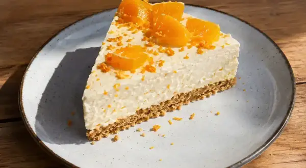 En bit krämig apelsincheesecake med kexbotten, toppad med apelsinklyftor och rivet skal. Ett perfekt cheesecake recept för fikat.