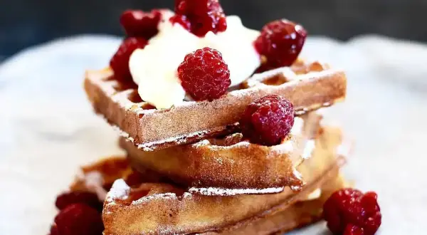 En stapel gyllene belgiska våfflor toppade med vispad grädde och färska hallon, pudrade med florsocker. En härlig frukost eller dessert.