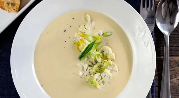 Krämig potatis och blomkålssoppa med garnering av blomkål, salladslök och peppar. Serveras med en bit rostat bröd.