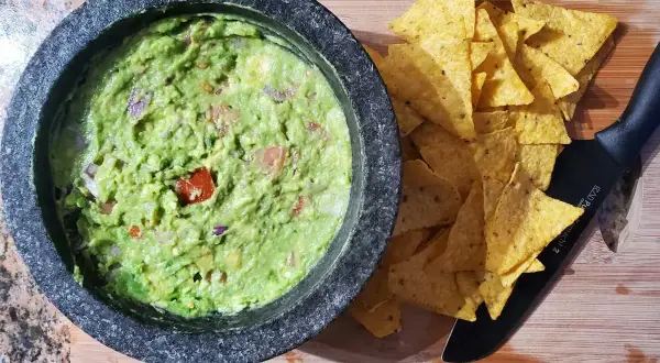 Närbild på en skål med hemgjord guacamole, perfekt för ett enkelt guacamole recept. Tortillachips och en kniv ligger bredvid.
