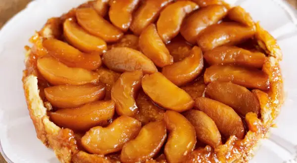 En gyllene tarte tatin med karamelliserade äppelklyftor som glänser. En klassisk fransk dessert som ser utsökt ut.