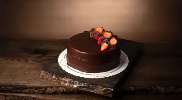 En lyxig fransk chokladtårta med färska bär och chokladdekorationer, serverad på en rustik träbricka.