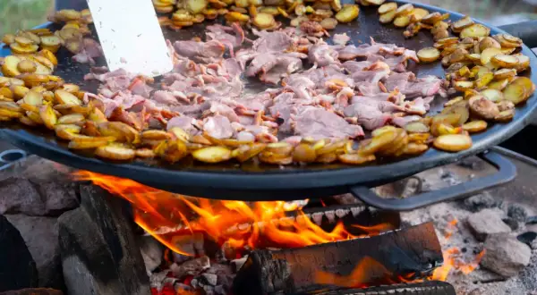 Kött och potatis steks på en Muurikka över öppen eld. Ett perfekt recept för utomhusmatlagning.