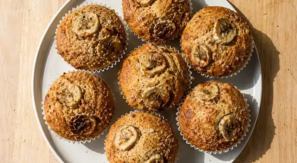 Sju gyllene bananmuffins med skivor av banan på toppen, redo att avnjutas. Ett perfekt bananmuffins recept för fika.