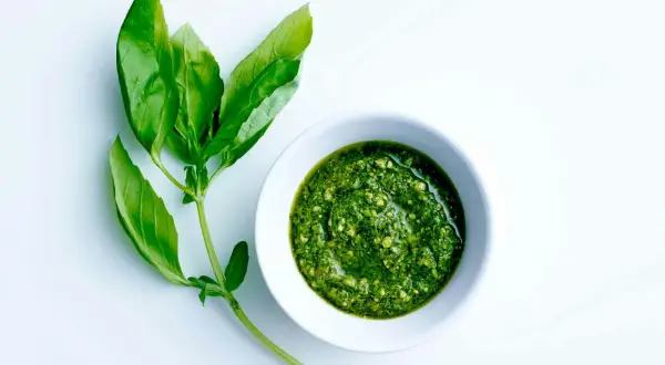 En skål med grön pesto bredvid färska basilikablad. Perfekt för ett enkelt pesto recept.