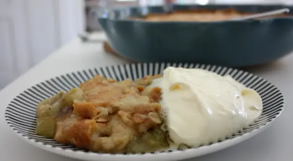 En portion rabarberpaj med kardemumma och en klick grädde på en randig tallrik.