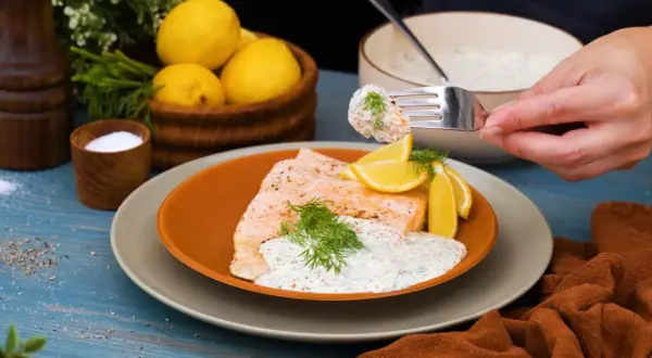 En bit lax med citron och dill, toppad med en krämig klassisk romsås. En gaffel med sås och rom lyfts från skålen.