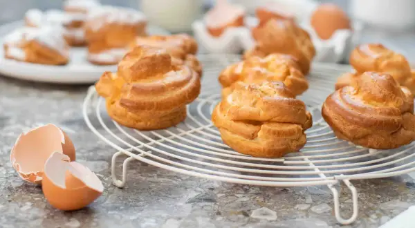 Nybakade petit choux på ett galler, med äggskal i förgrunden. Perfekt för en fika!