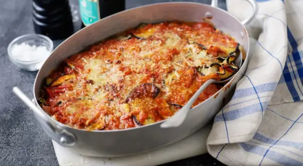 En ugnsform med en gyllene, bubblande melanzane alla parmigiana, toppad med riven ost och tomatsås. En klassisk italiensk rätt som doftar ljuvligt.