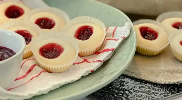 Glutenfria hallongrottor med sylt på en ljusgrön tallrik, bredvid en skål med hallonsylt och en sked.