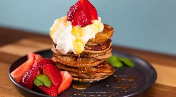 En stapel bananpannkakor med vispgrädde, jordgubbar och sirap. Ett perfekt bananpannkaka recept för frukost eller brunch.