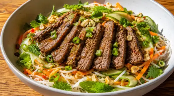 En läcker asiatisk biffsallad med tunt skivad biff, nudlar, gurka, morötter, mynta och jordnötter i en skål.