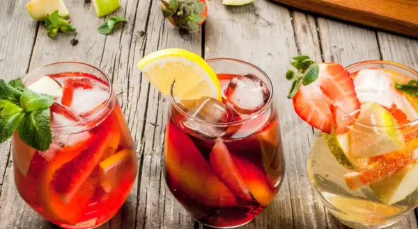 Tre glas med färgglad sangria, fyllda med frukt och is. Perfekt för ett somrigt recept sangria.