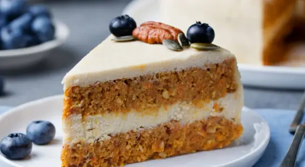 En saftig bit vegansk morotskaka med krämig frosting, toppad med blåbär och pekannöt. En härlig fika!