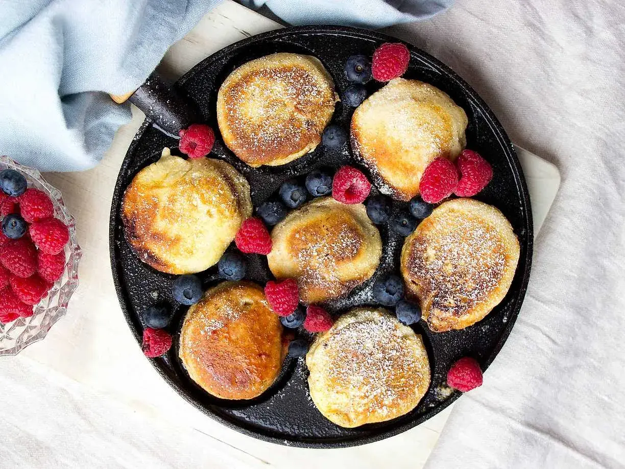 Små, gyllene pannkakor med pudersocker och bär, redo att avnjutas. Ett perfekt krabbelurer recept för frukost eller fika.