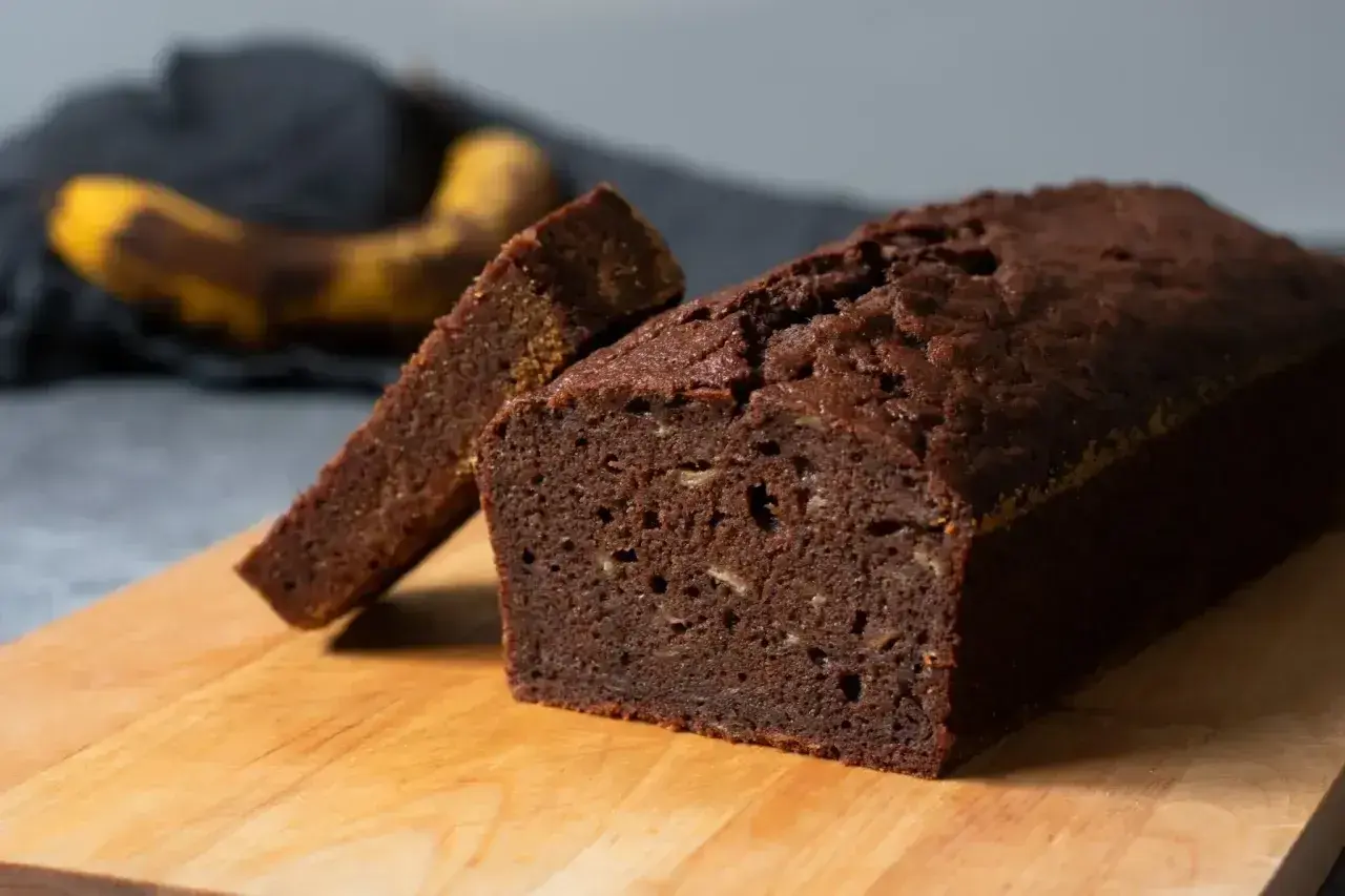 En saftig banankaka i sockerkaksform, med en skiva upplagd. En övermogen banan ligger i bakgrunden.