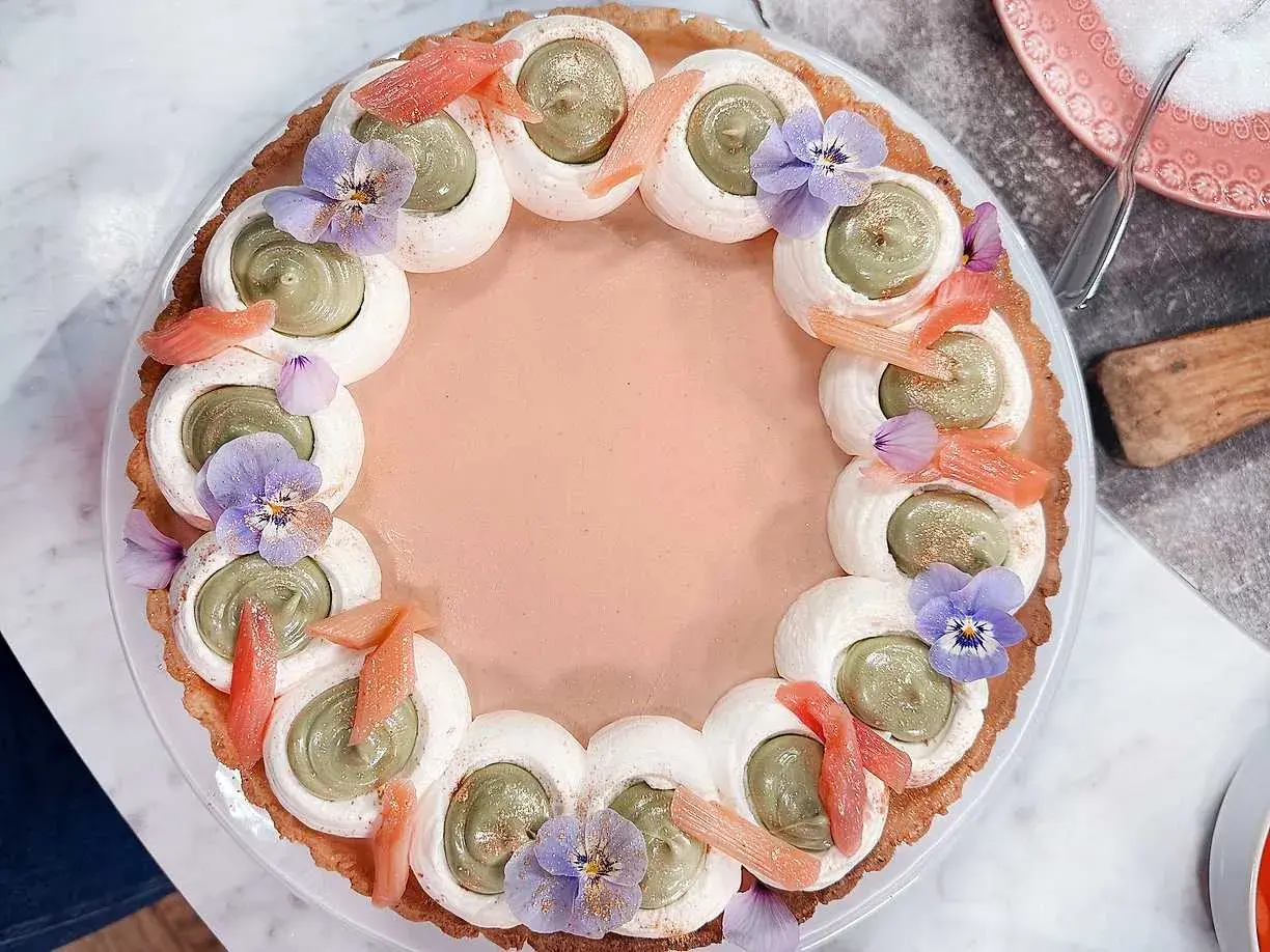En vacker pannacotta med rabarber, dekorerad med grön kräm, maräng, violer och rabarberbitar.