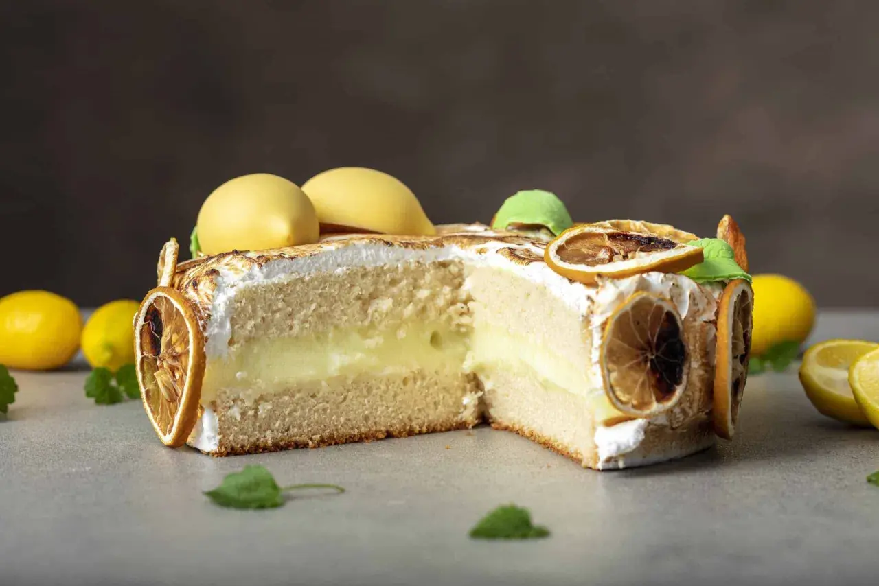 En skivad citron tarte med fluffig maräng, krämig fyllning och dekorerad med torkade citronskivor och gula marängkulor.