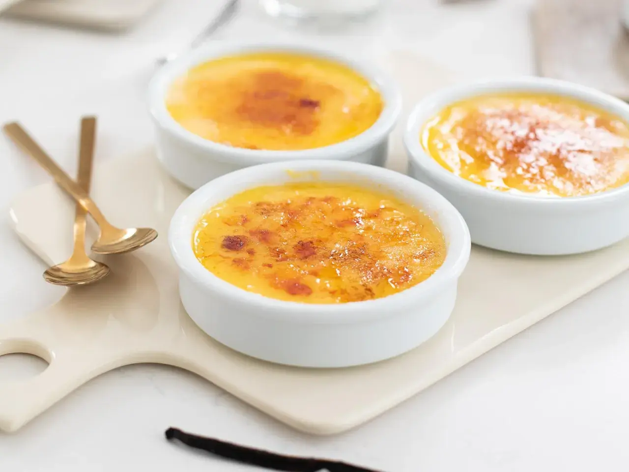Tre krämiga crème brûlée i vita skålar med karamelliserat socker. Perfekt för ett enkelt creme brulee recept.