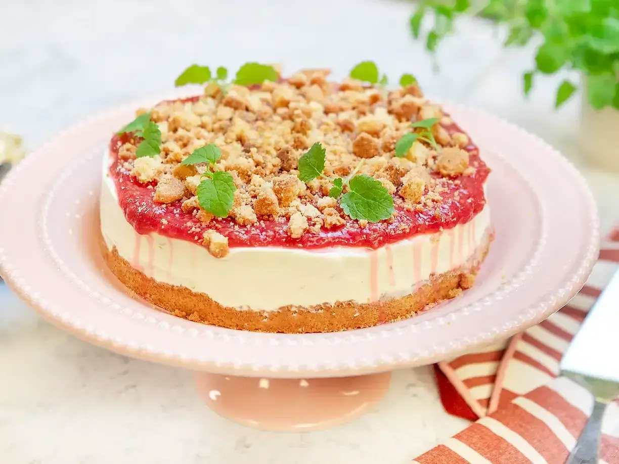 En läcker rabarber cheesecake med smulig topping och myntablad, serverad på ett rosa tårtfat.