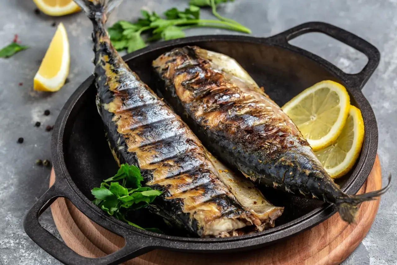 Två saftiga, grillade makrillar serveras i en gjutjärnspanna med citronklyftor och persilja. Perfekt för en somrig middag.