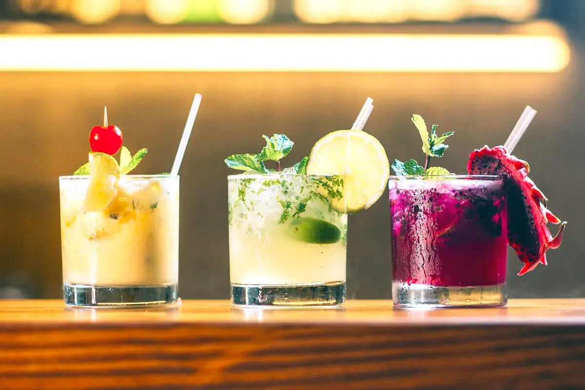 Tre färgglada alkoholfria drinkar med frukt och mynta på en träbar.