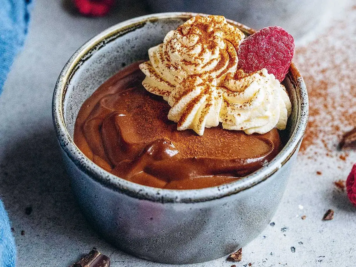 En krämig chokladpudding i en skål, toppad med vispad grädde, hallon och kanel. Perfekt för ett chokladpudding recept.
