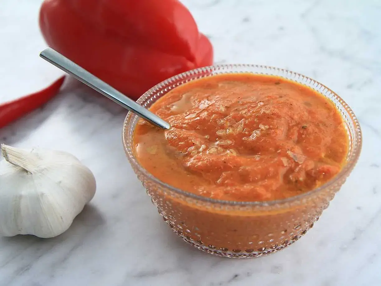 En skål med ajvar relish, en röd paprika, en chili och ett vitlökskläpp.