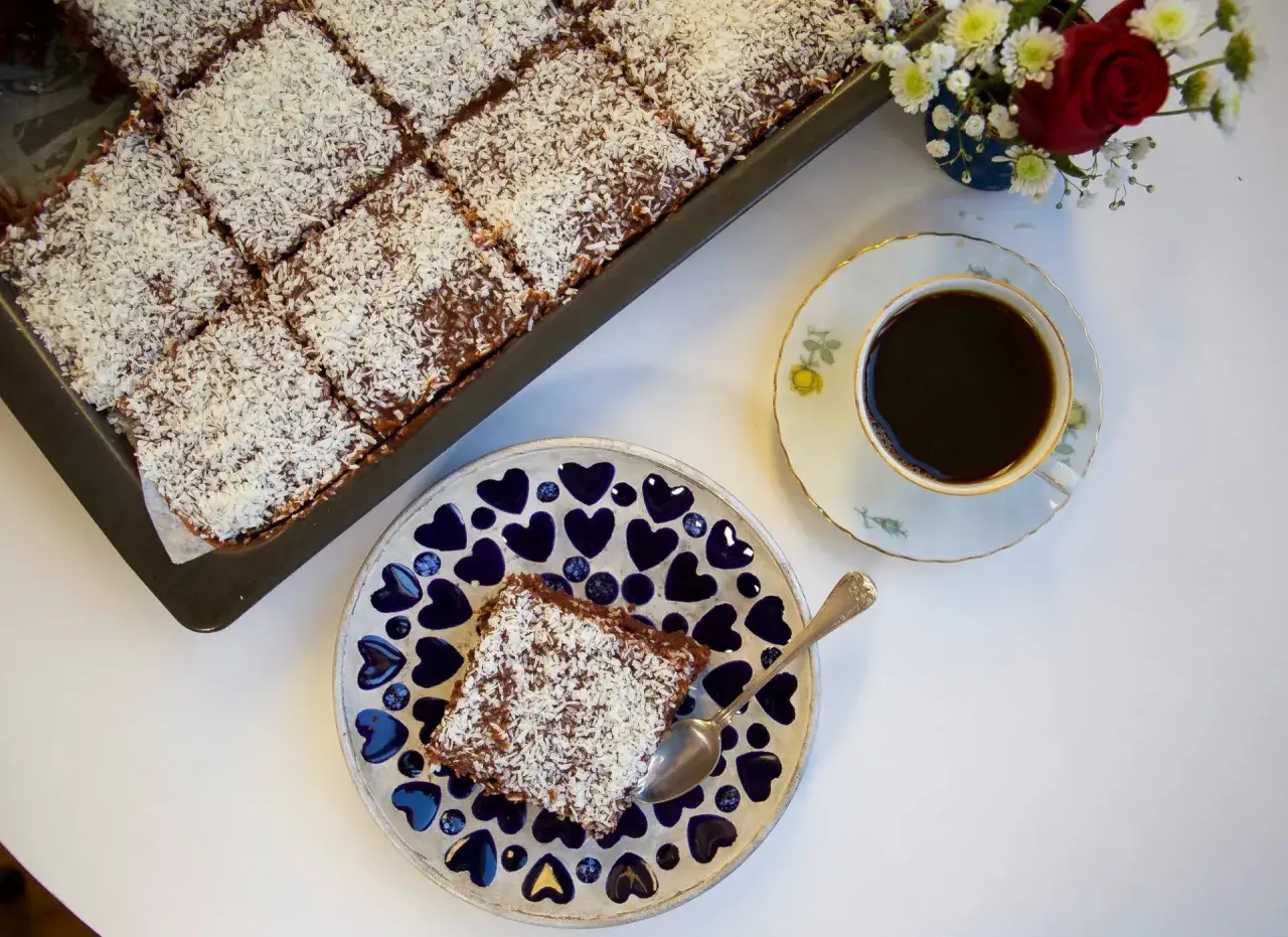 En saftig citronkaka i långpanna, toppad med kokosflingor, serveras med en kopp kaffe.