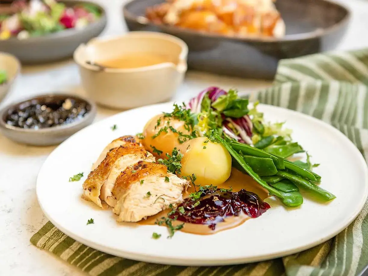 En saftig hel kyckling i ugn, skuren och serverad med potatis, sockerärtor och en härlig lingonsylt.