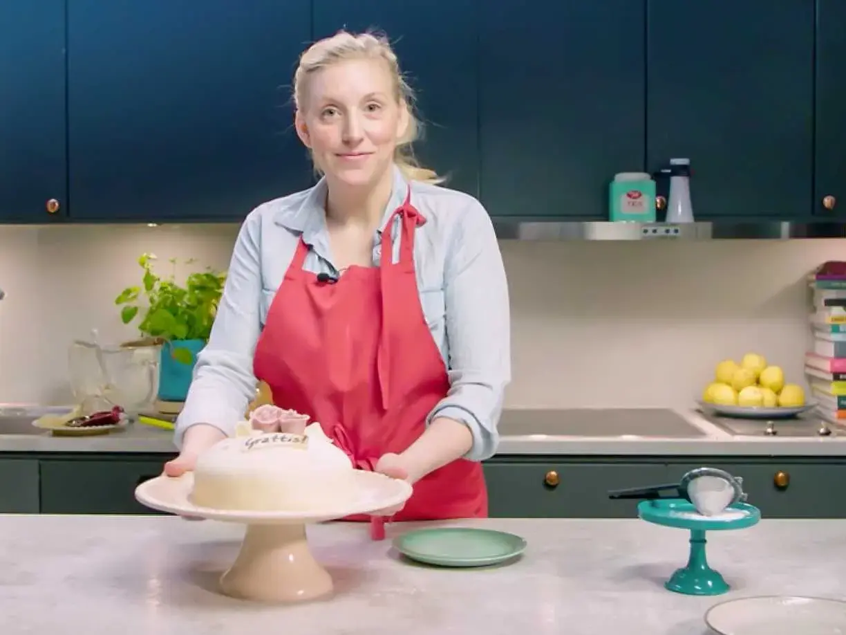Kvinna med röd förkläde presenterar en marsipantårta. Ett perfekt marsipan recept för firande.