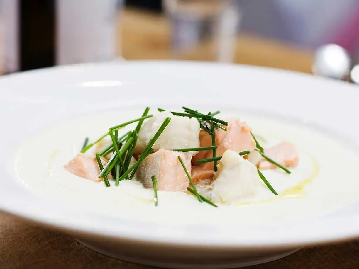 En krämig soppa med bitar av confiterad lax och vit fisk, toppad med färsk gräslök.