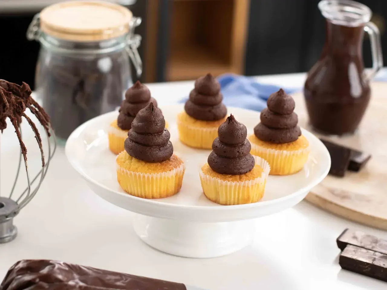 Fem cupcakes med chokladganache, perfekt för ett enkelt ganache recept. Ingredienser för bakning syns i bakgrunden.