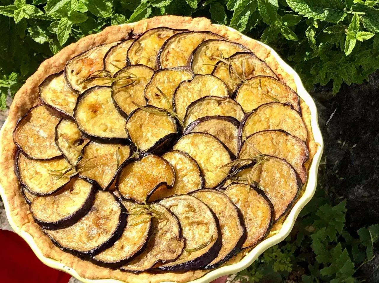 En paj med gyllene, stekt aubergine och rosmarin, vackert arrangerad i en ljusgul form.