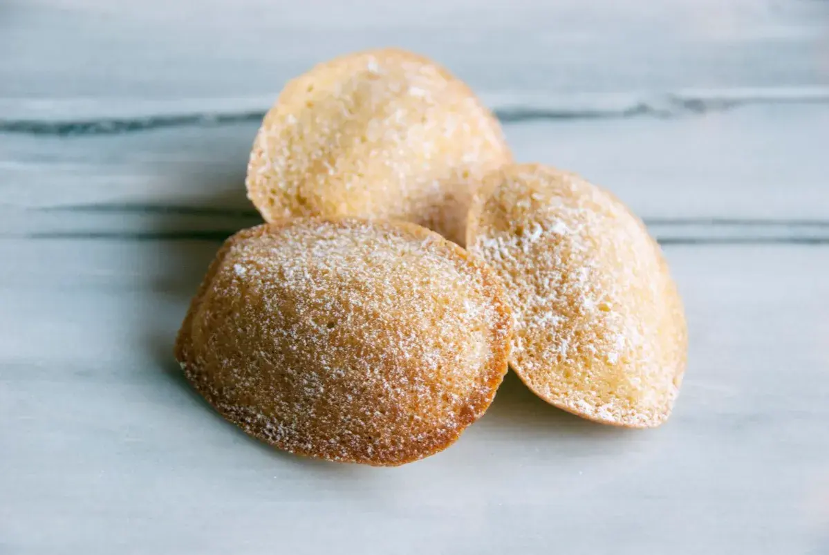 Tre gyllene madeleines, pudrade med florsocker, redo att avnjutas. Ett enkelt och gott madeleine recept.
