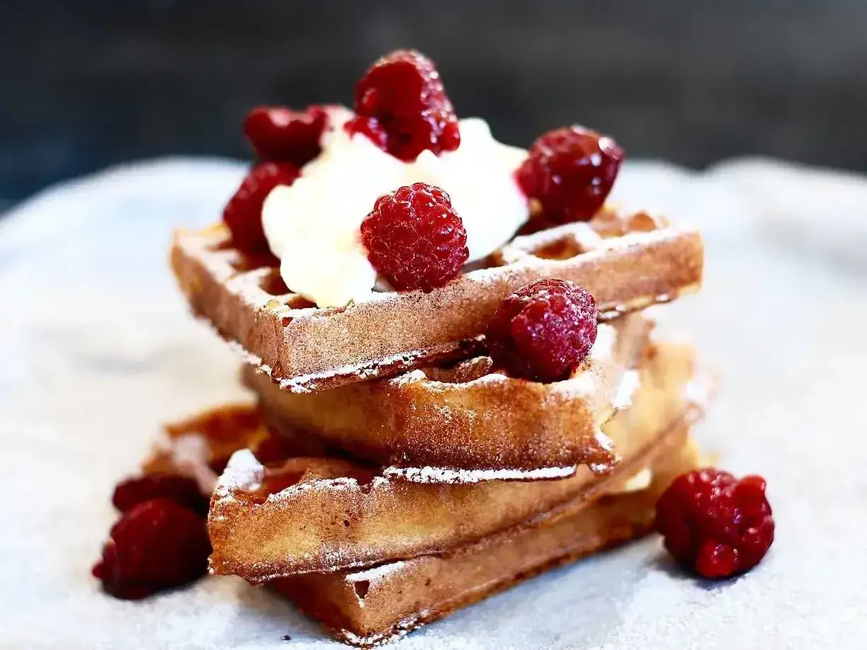 En stapel gyllene belgiska våfflor toppade med vispad grädde och färska hallon, pudrade med florsocker. En härlig frukost eller dessert.