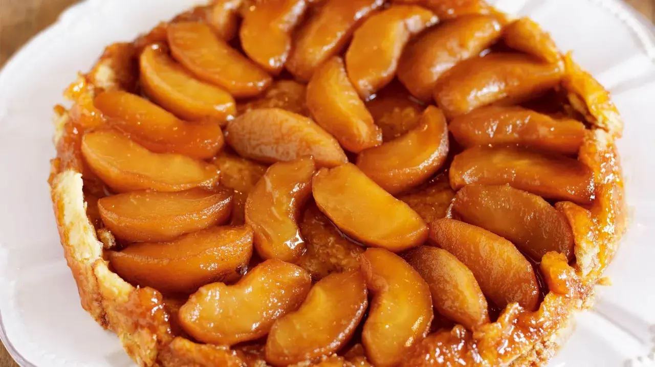 En gyllene tarte tatin med karamelliserade äppelklyftor som glänser. En klassisk fransk dessert som ser utsökt ut.