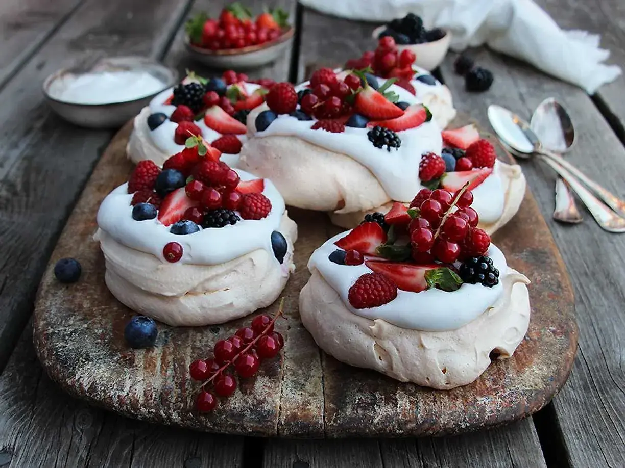 Små pavlova med grädde och färska bär som jordgubbar, hallon, blåbär och vinbär. En härlig sommardessert.