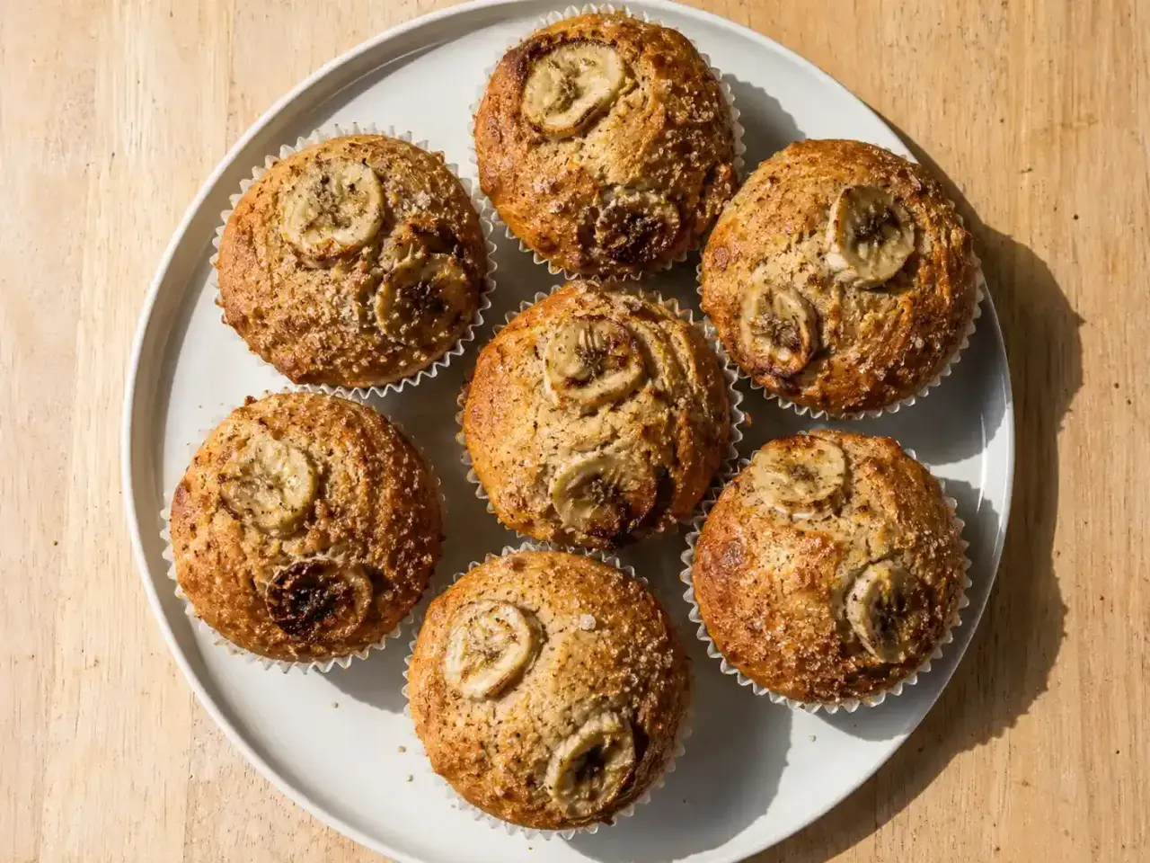 Sju gyllene bananmuffins med skivor av banan på toppen, redo att avnjutas. Ett perfekt bananmuffins recept för fika.
