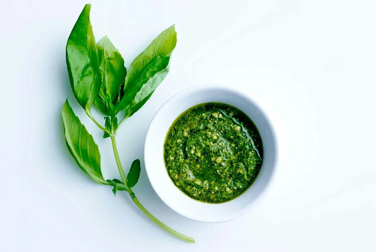 En skål med grön pesto bredvid färska basilikablad. Perfekt för ett enkelt pesto recept.