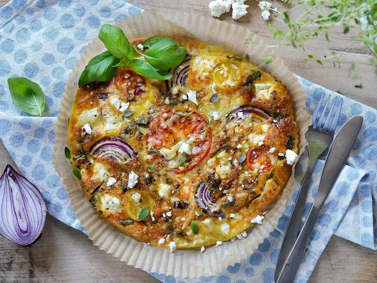 En gyllene omelett i airfryer med tomat, rödlök och fetaost, toppad med färsk basilika. Perfekt för en snabb och god måltid.