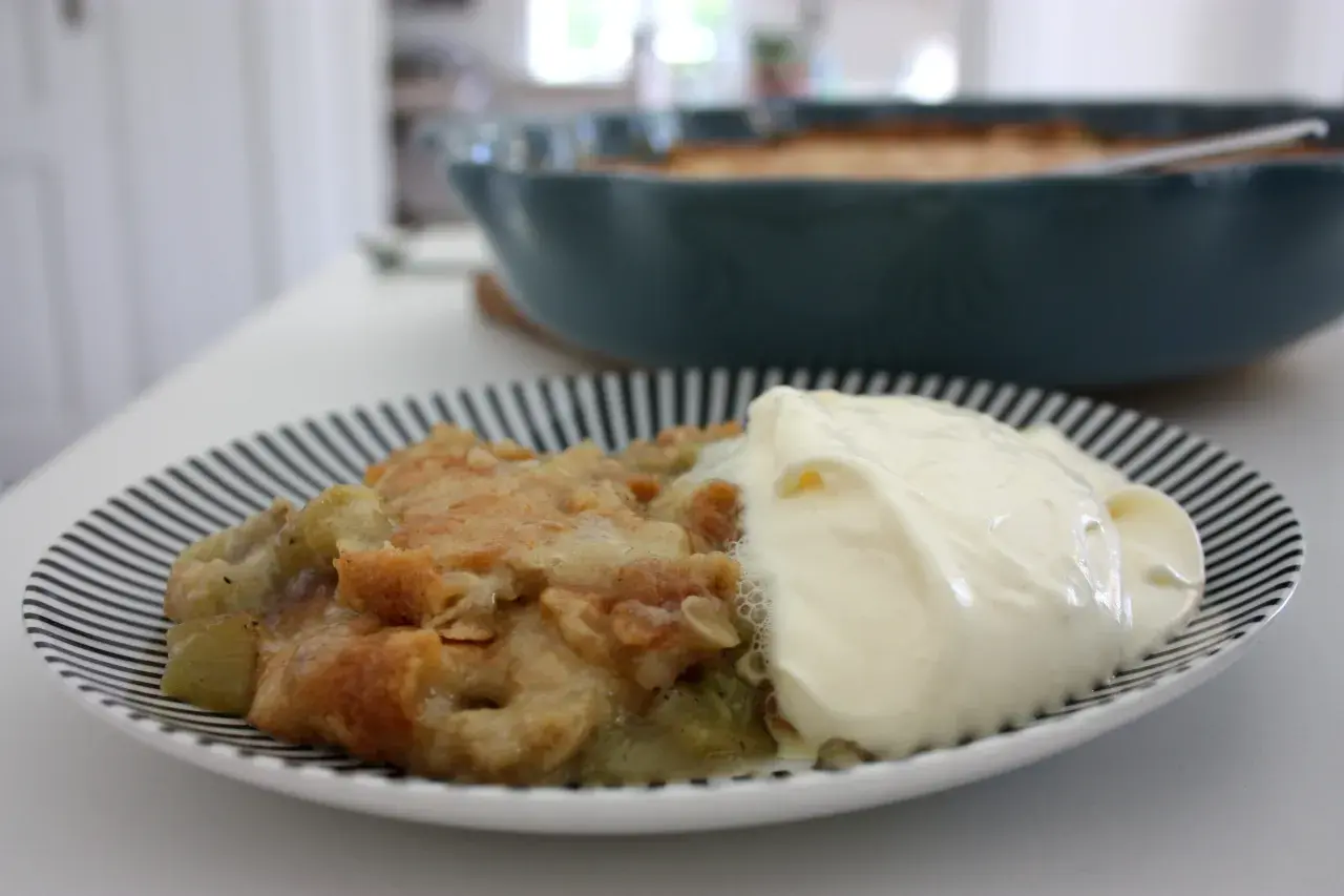 En portion rabarberpaj med kardemumma och en klick grädde på en randig tallrik.